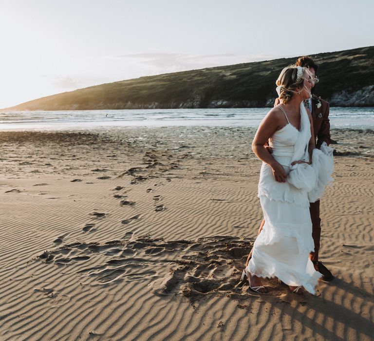 Bride & groom walk along the beach with one another in Cornwall