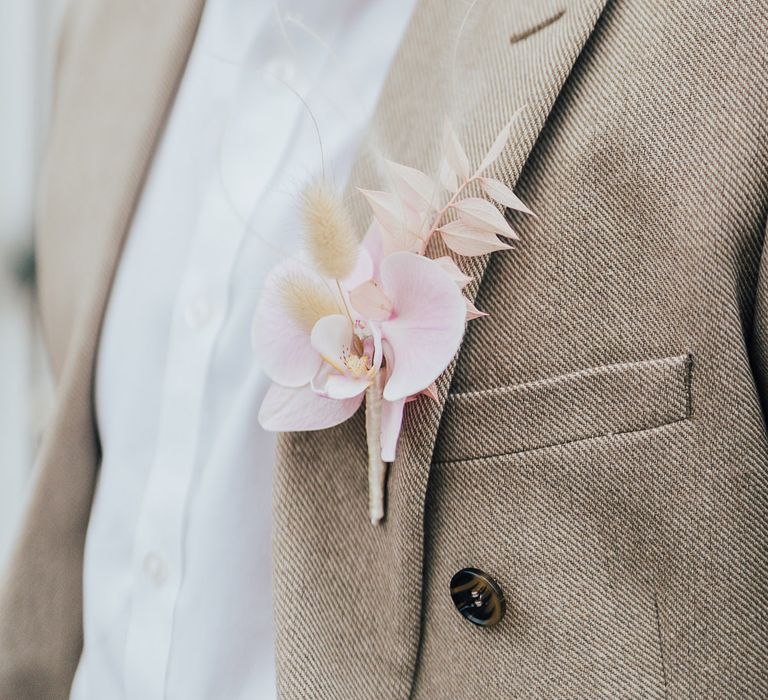 Groom in a beige suit with pink orchid buttonhole 