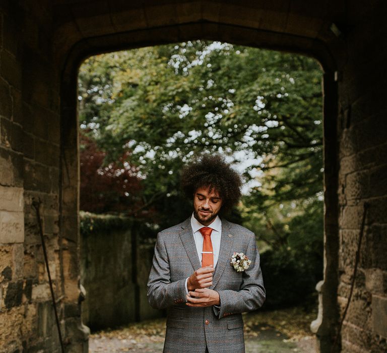 Black groom with afro hair in a grey wedding suit with orange check design and tie