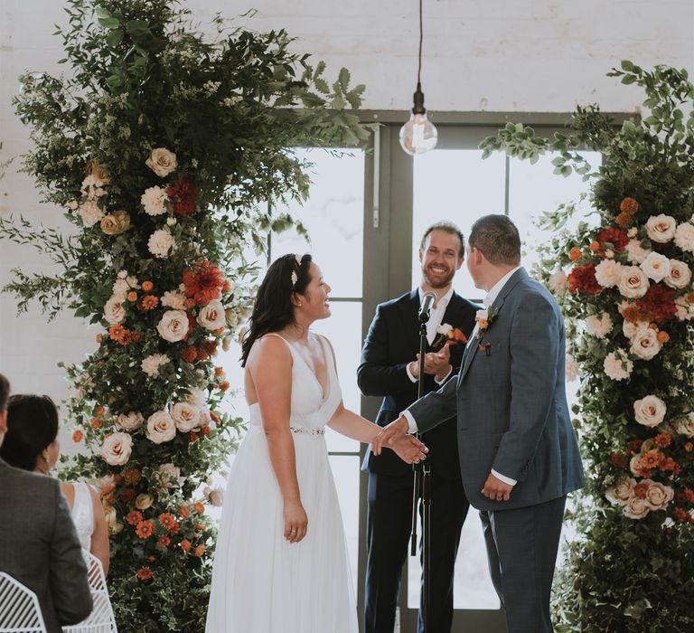 Bride and groom holding hands at the altar decorated with vertical floral arrangements 