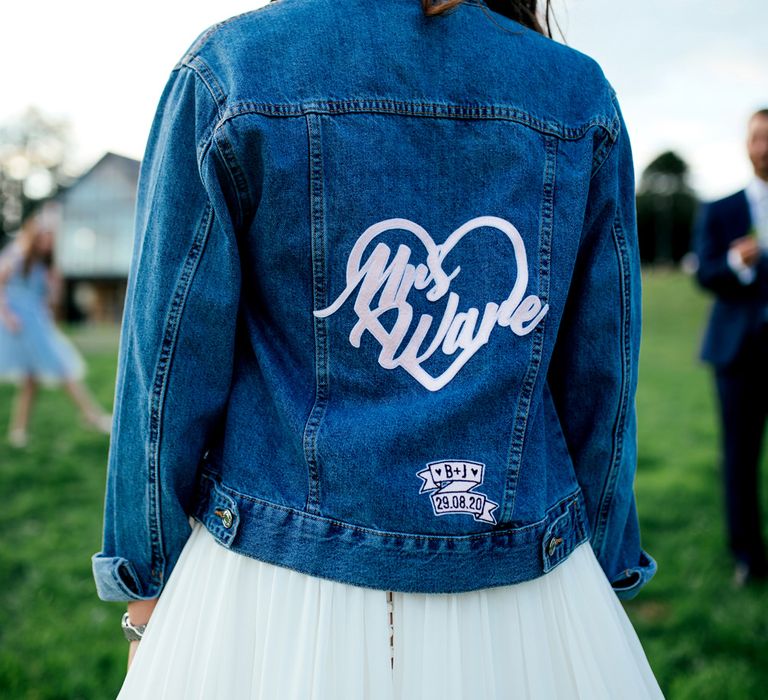 Bride in a personalised denim jacket with the brides new married name in a heart and the wedding date on a scroll  