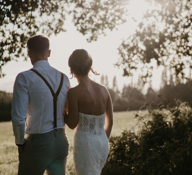 Bride & groom walk together across field as the sun begins to set on their wedding day | Mark Bamforth Photography