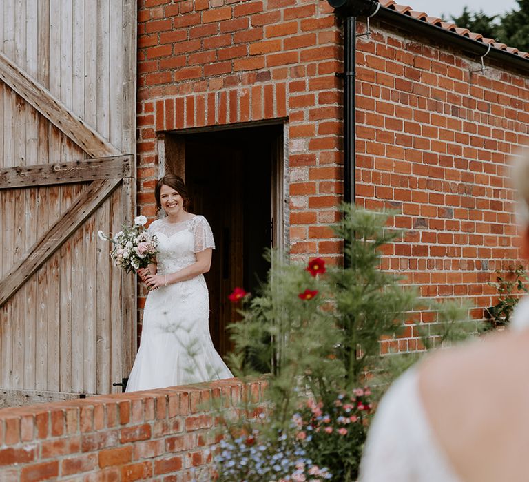 First look with bride in an embellished wedding dress holding a white and pink wedding bouquet approaching her bride with short hair 