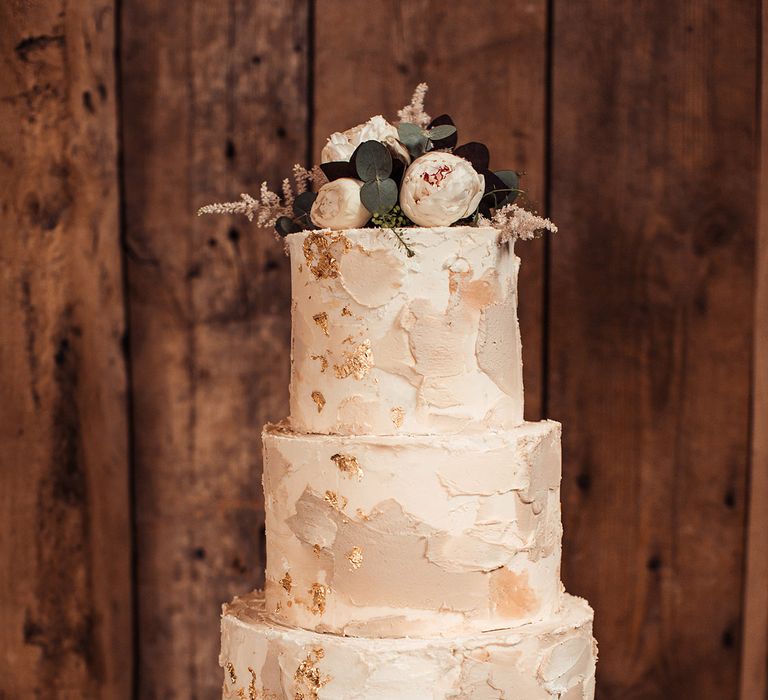 Three tier wedding cake with gold leaf decor and close peony flower cake topper decoration 