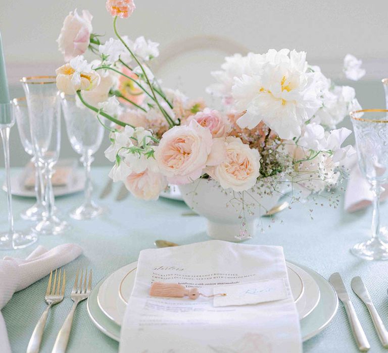 Place setting with pale green tablecloth, gold rimmed glasses and tableware, and floral centrepiece 