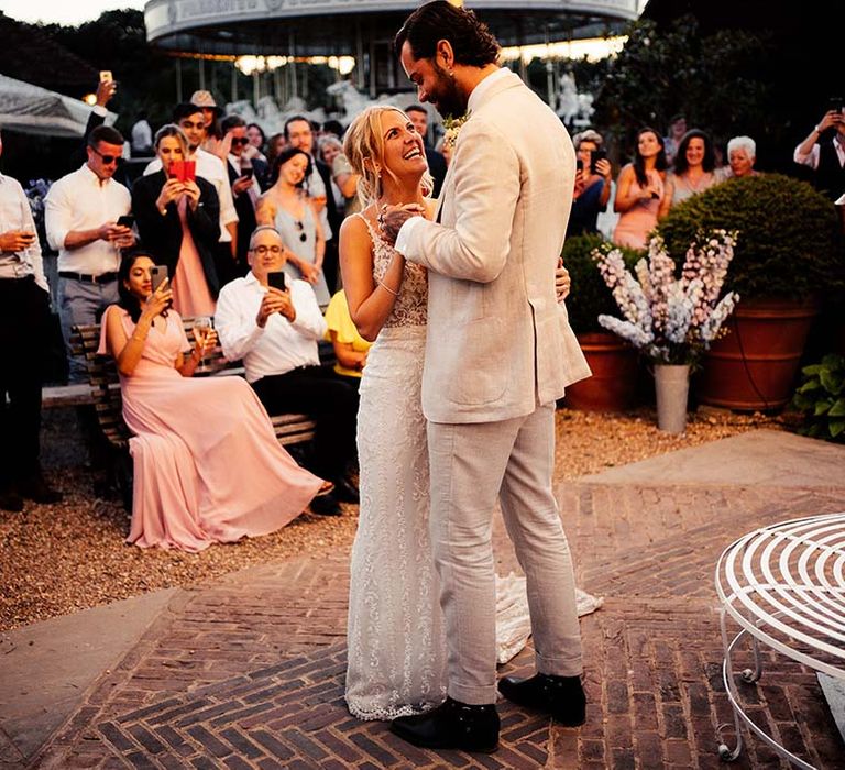 Groom in a beige suit dancing with his bride in a fitted lace wedding dress