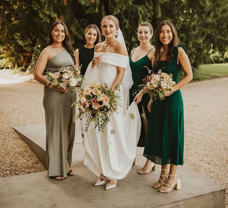 Bride stands with her bridesmaids who wear green bridesmaids gowns in different shades and styles