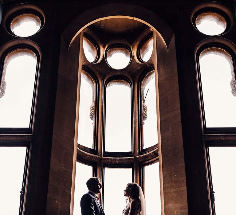 Bride & groom stand in front of impressive windows on their wedding day