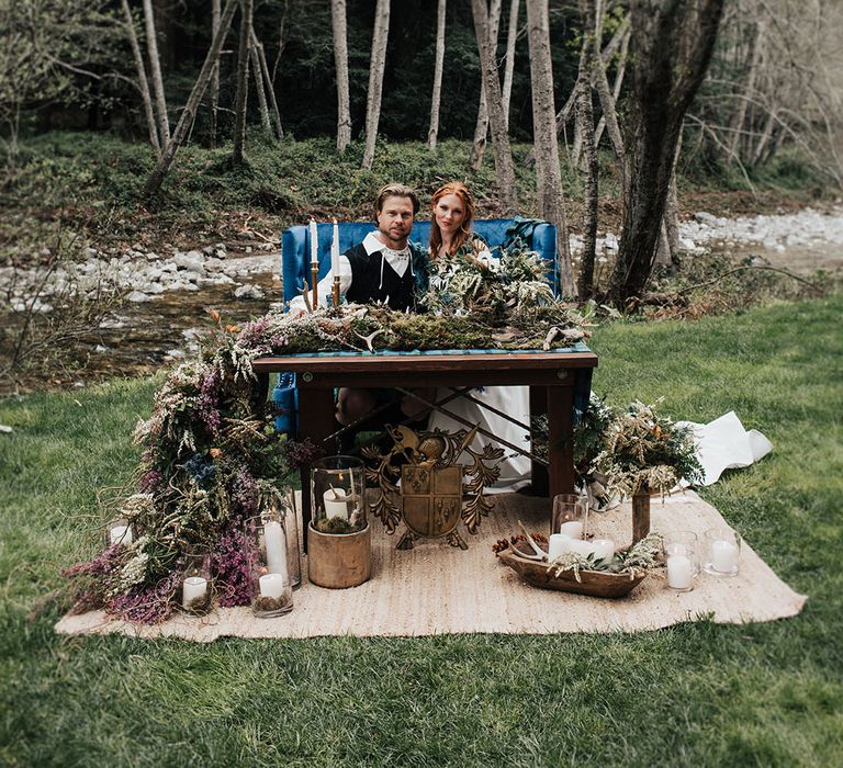 Bride with red hair and groom sitting at their outdoor boho sweetheart table 