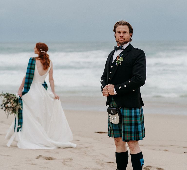 Groom in a blue and green tartan kilt wearing a sporran and black jacket on the beach at Big Sur