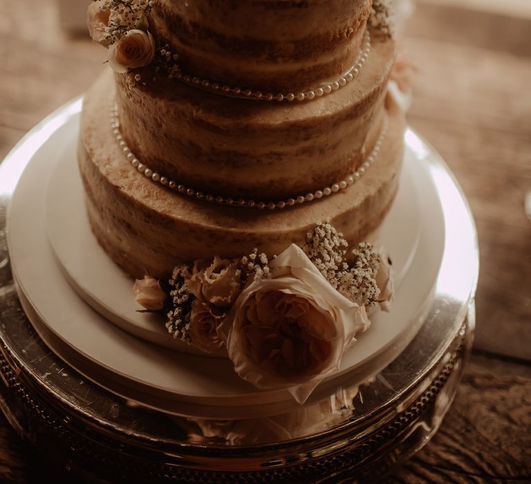 Three tier naked wedding cake decorated with pearls and fresh flowers 