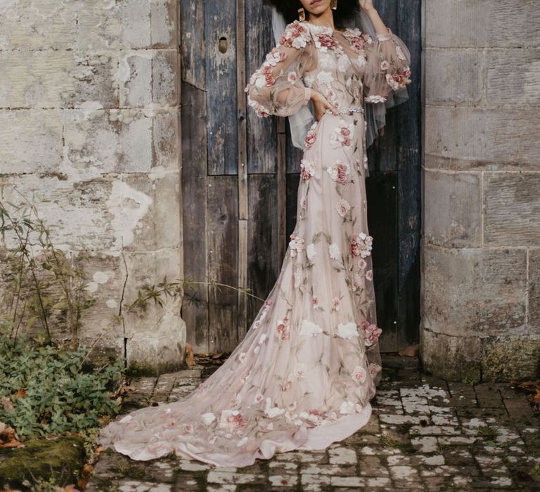 Black bride in a 3D flower appliqué pink embroidered wedding dress with sheer long sleeves and puddle train at Chiddingstone Castle wedding venue in Kent 