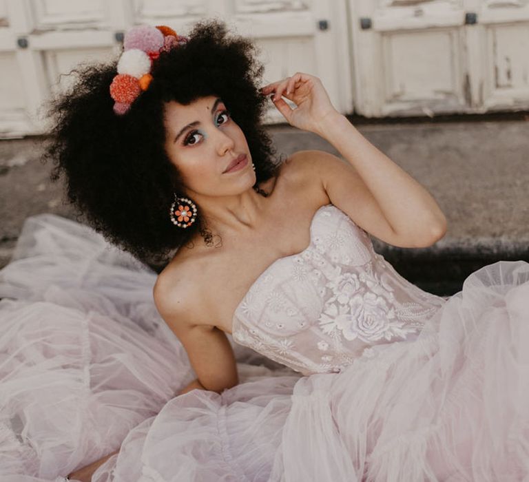 Black bride with afro hair wearing a pompom headdress, clay earrings and a corset top