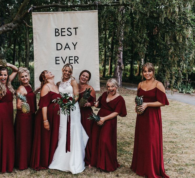 Bride stands in wood with bridesmaids in burgundy bridesmaid dresses from Rewritten