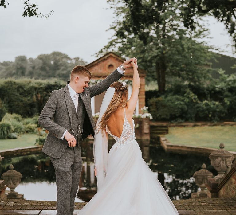 Groom in grey tweed suit spins around bride in tulle skirt at country house rustic wedding venue