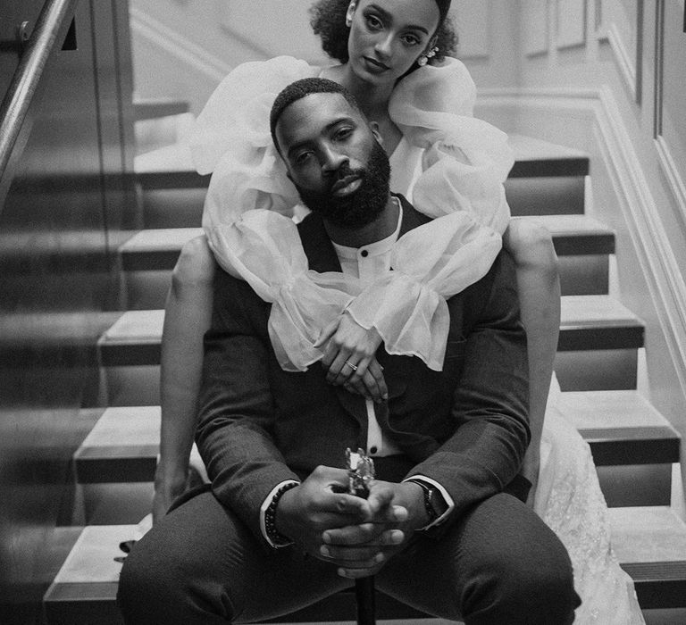 Black bride with an afro middle parting wedding ponytail embracing her husband on the steps at Mayfair Townhouse 