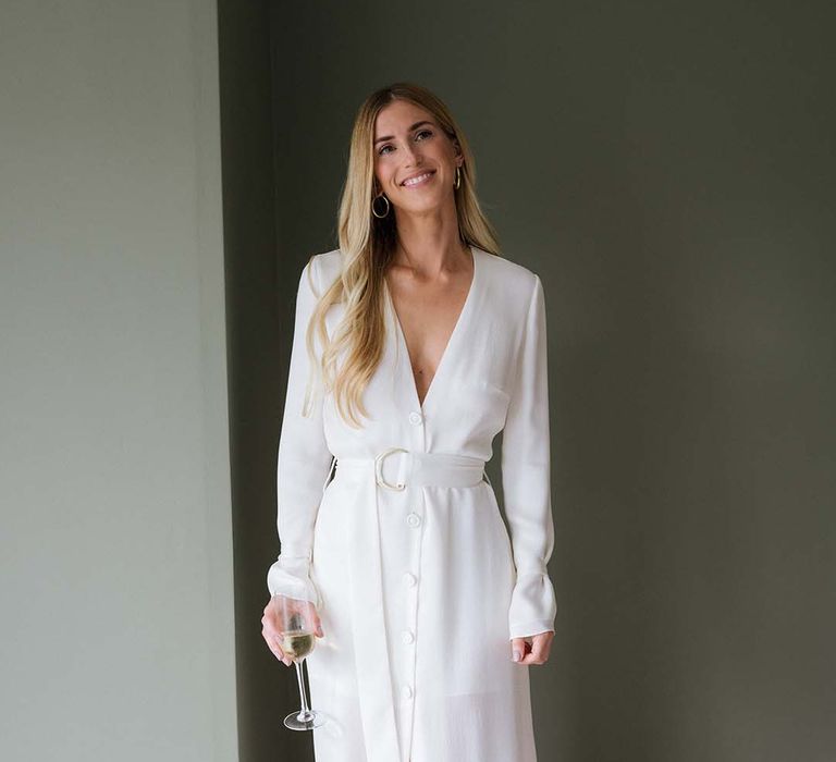 Bride's relaxed white long sleeve and plunging neckline buttoned wedding dress with belt and gold Saint Laurent mules 