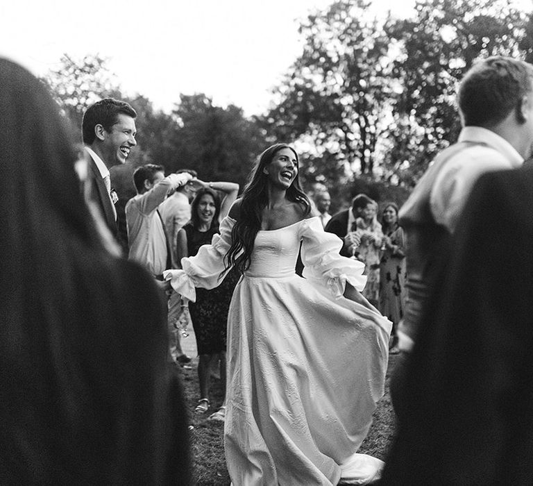 Bride in off the shoulder textured Emma Beaumont wedding dress dancing outside