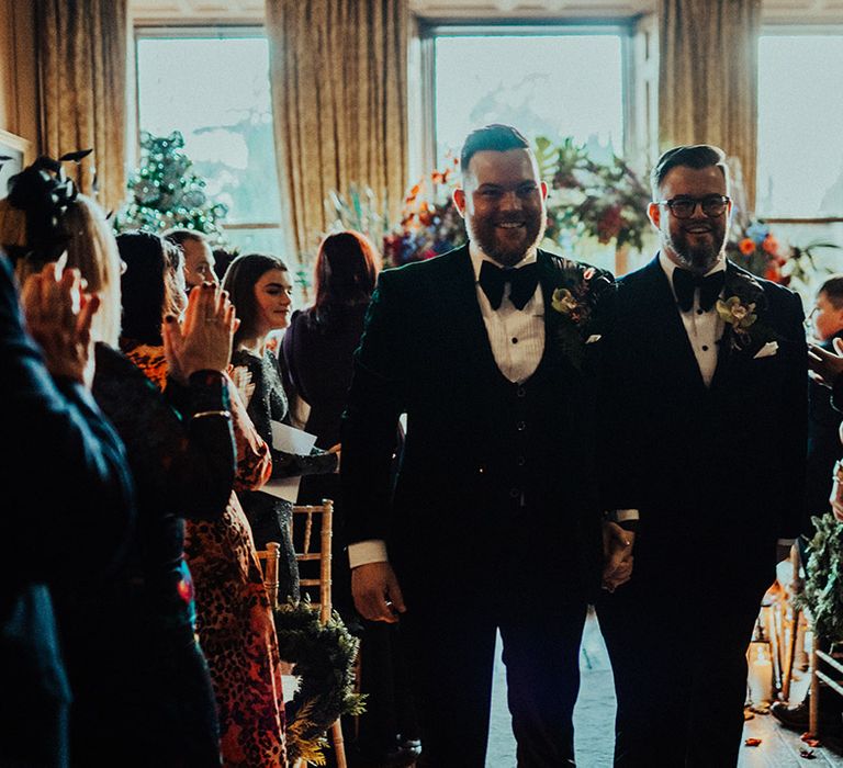 Grooms walk back down the aisle together as a married couple as the guests applaud them