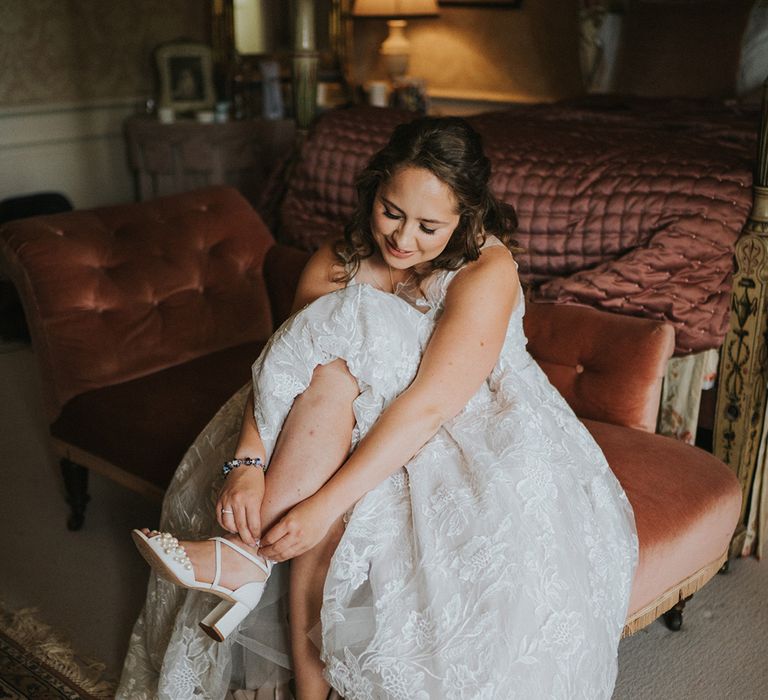 Bride in lace wedding dress puts on her pearl wedding shoes for her big day