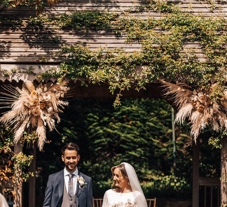 Bride holding hands with groom under archway at outdoor ceremony at Pennard House