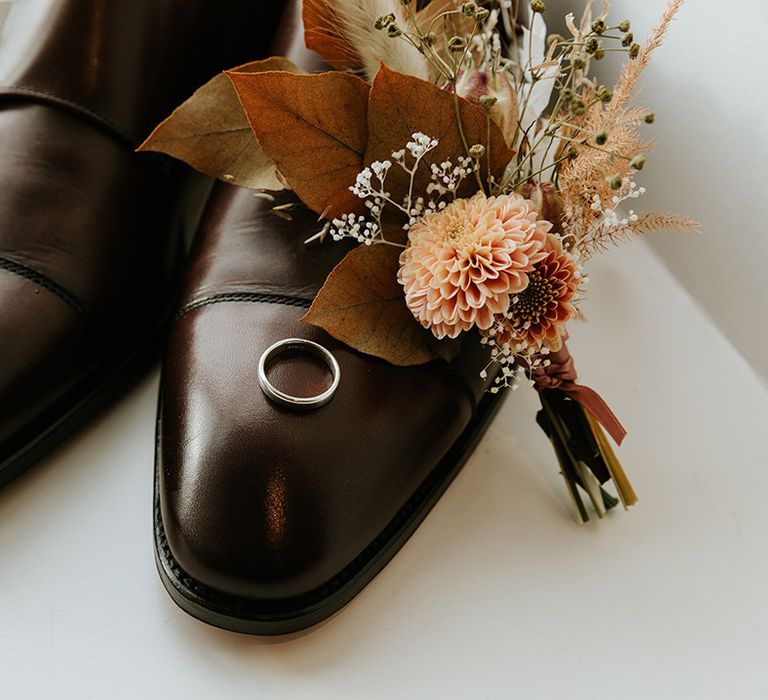 Groom's brown shows with the wedding bands on each shoes and small autumnal bouquet