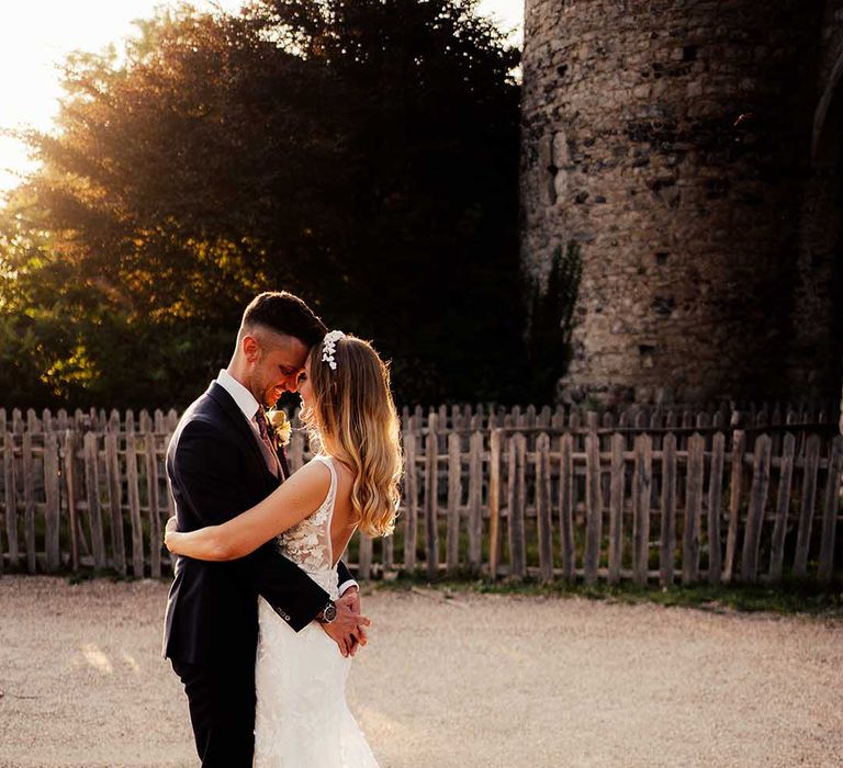 Bride and groom hug with bride in lace dress with sheer train at the Cooling Castle wedding venue