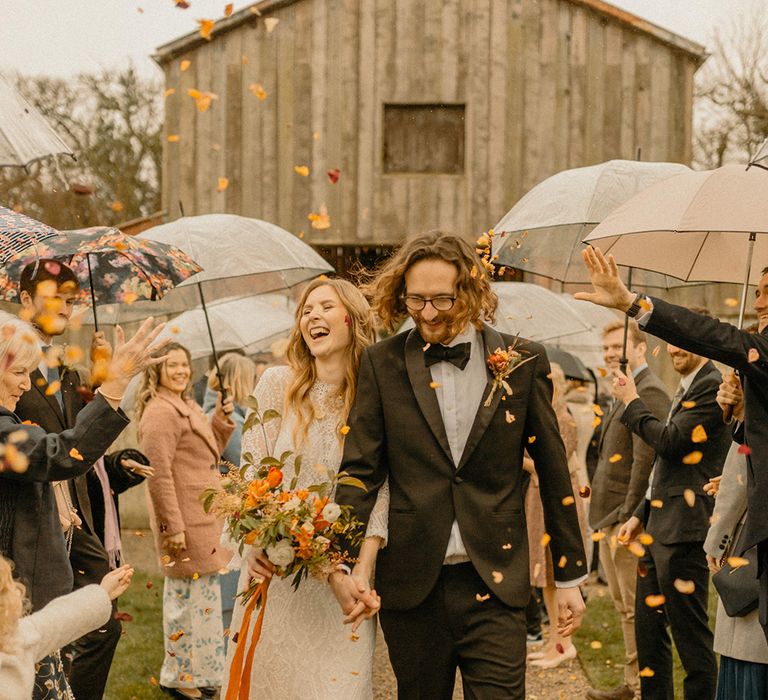 Groom in black tie has orange confetti exit with bride in lace wedding dress