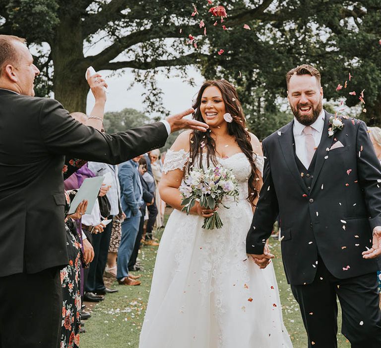 Bride and groom exit their outdoor wedding ceremony to pink confetti being thrown over them