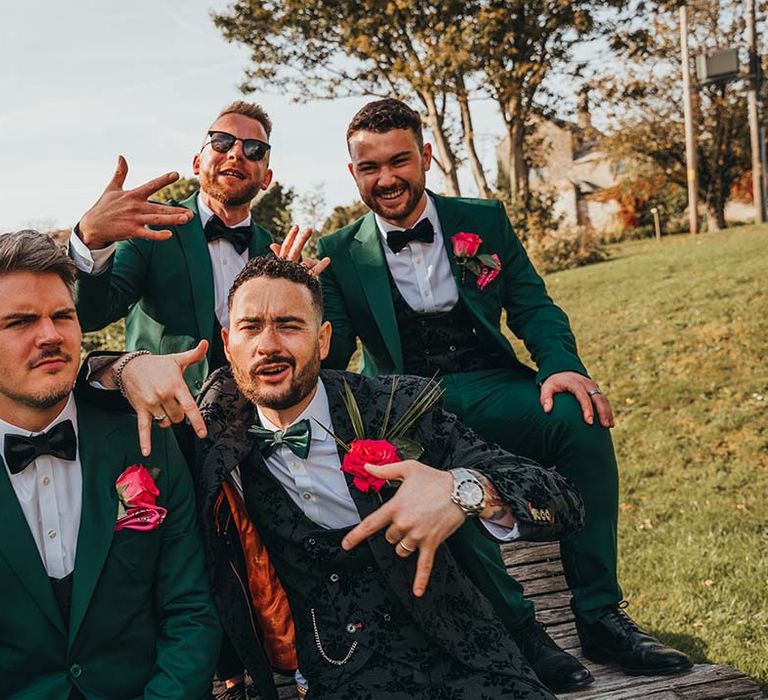 Groom poses with his groomsmen in matching emerald green and black patterned suit colours for wedding day