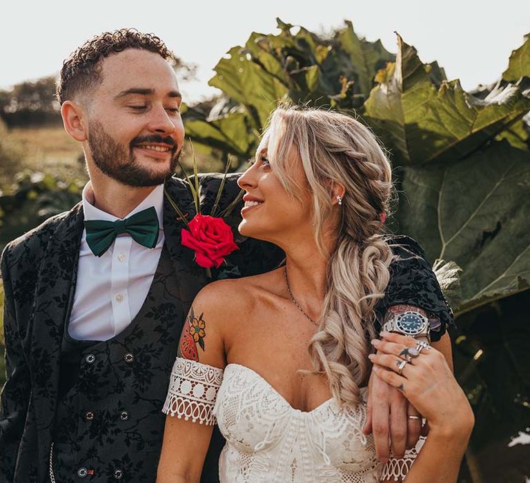 Bride in strapless lace boho wedding dress with groom in black patterned three piece suit