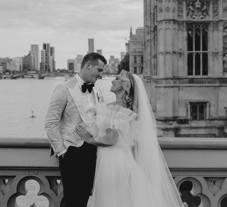 Bride smiles as she stands with groom on bridge in ruffle style wedding dress 