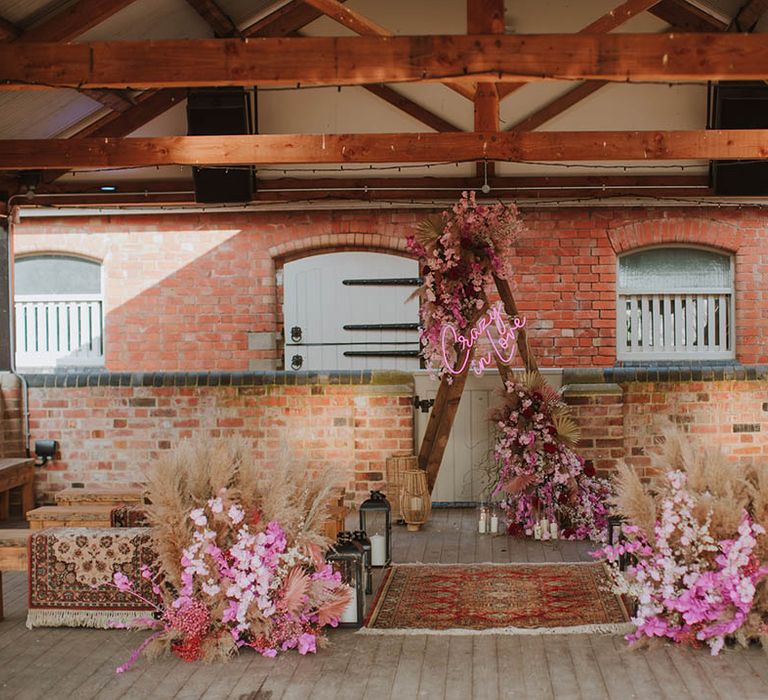 Aisle and altar style at Prestwold Hall Barns wedding venue in Leicestershire with wool rugs, dried grasses, pink cherry blossom, lanterns and a wooden triangle frame. 