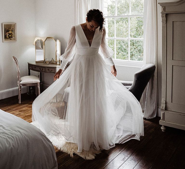 Bride in sheer long sleeve Sassi Holford wedding dress with tulle skirt and button detail 