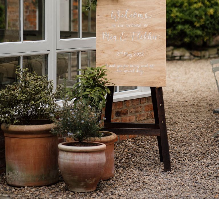 Wooden welcome wedding sign with white font decorated with flowers and greenery 