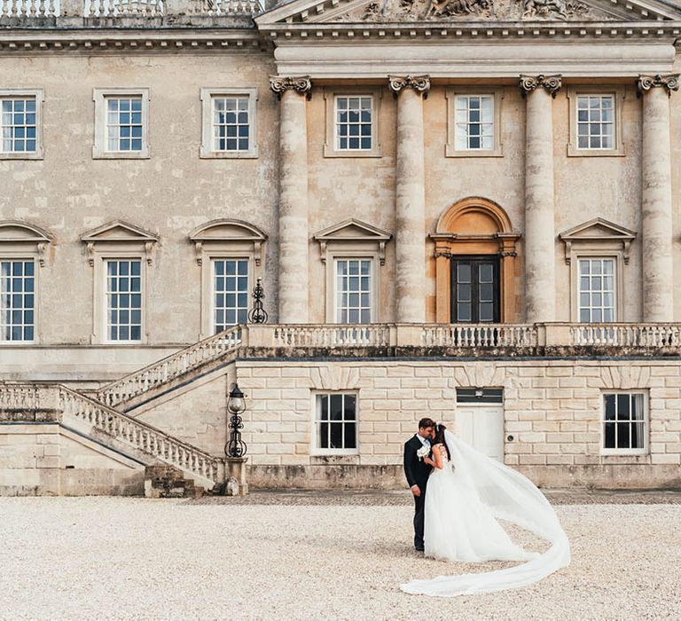 Bride and groom kiss in front of their luxe wedding venue, Kirtlington Park House