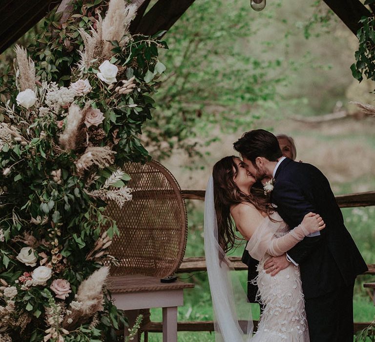 Bride and groom share their first kiss as a married couple next to flower column altar decoration 