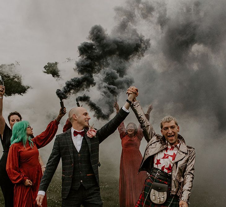 Grooms walk through grey smoke bombs held by their bridesmaids in deep red dresses 