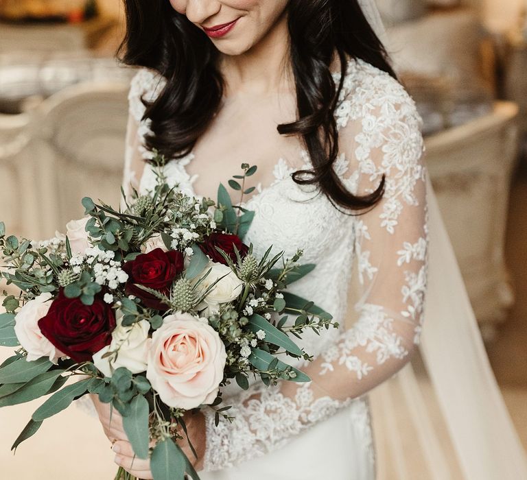 Bride wears red lipstick and her dark hair in loose curls complete with pearl hair accessory whilst holding white and red floral bouquet 