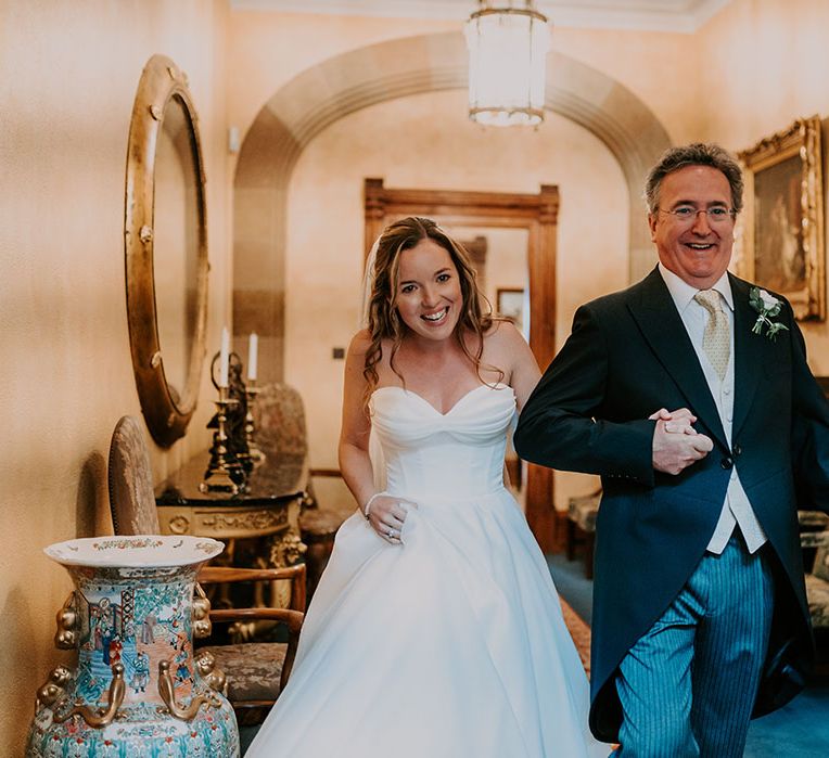 Bride wears sweetheart neckline Suzanne Neville wedding dress with full princess skirt whilst walking with her groom in traditional morning suit