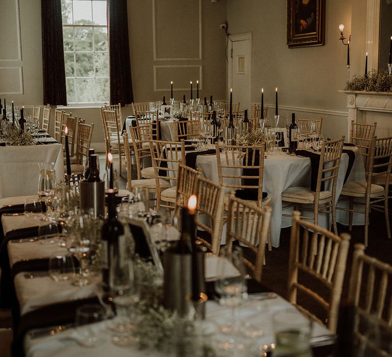 Chandelier hangs above round tables with white tablecloths, black pillar candles and black napkins 