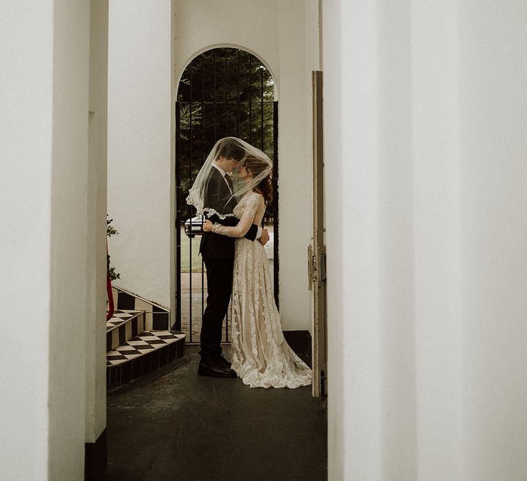 Bride wears lace edged veil and places it across herself and her groom during couples portraits at Belair House 