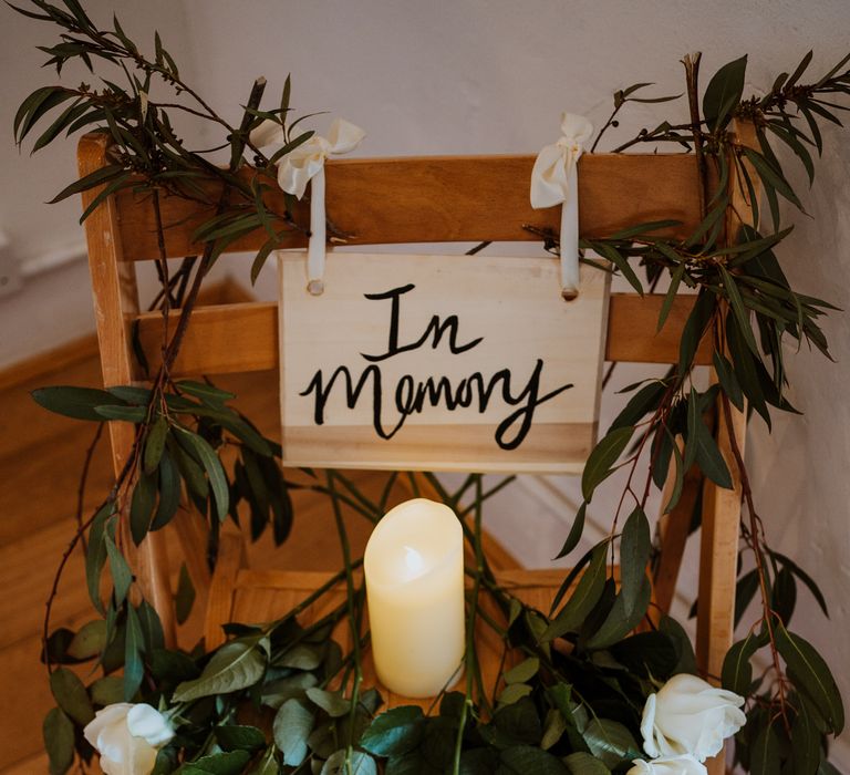 Wooden chair with DIY "In memory" sign, white long stemmed roses and a pillar candle