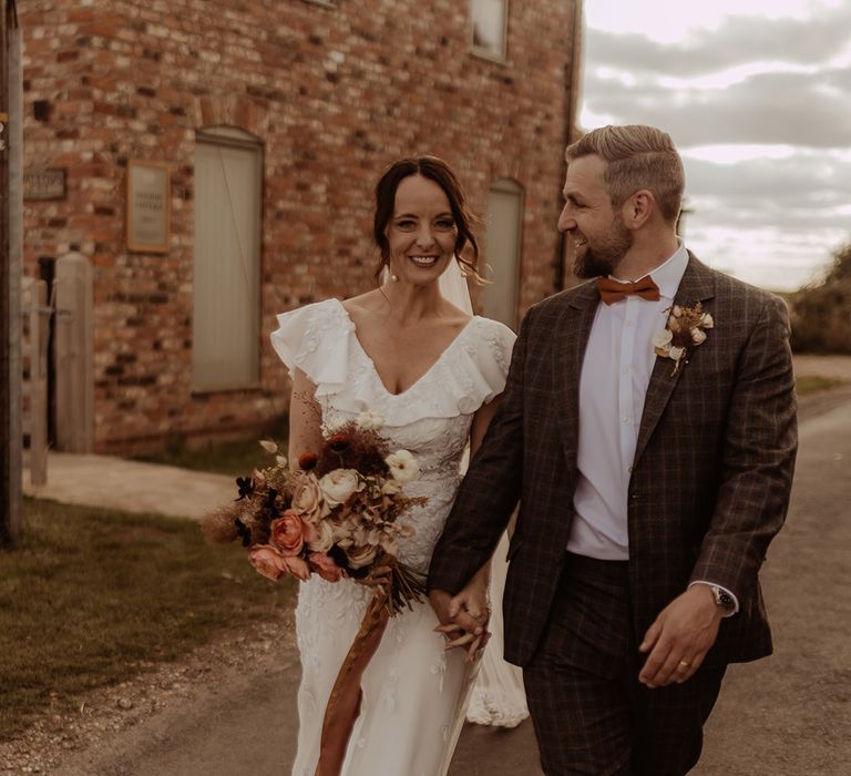 A ruffle floral embroidered Emma Beaumont Atelier wedding dress with the groom in a custom grey wedding suit 