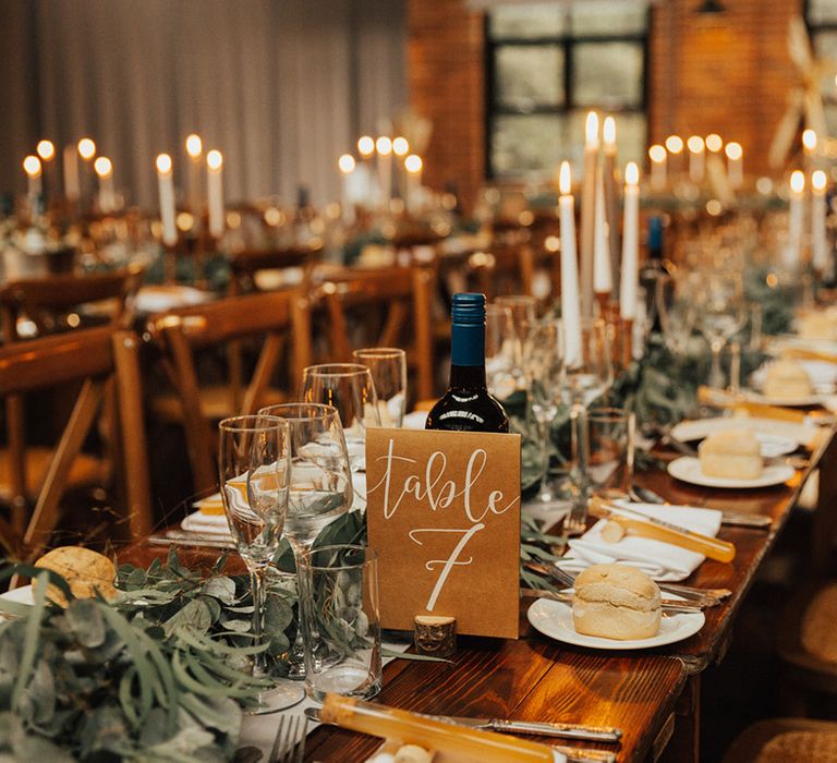 Wooden banquet table complete with neutral table runner and green foliage 