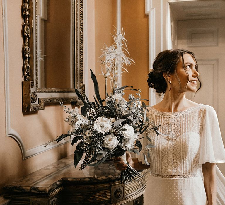 Bride in lace detailed batwing sleeve wedding dress holding neutral toned bridal bouquet with foliage decorations in Kelmarsh Hall classic wedding