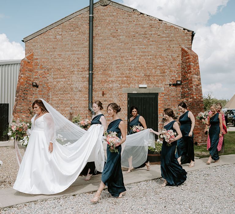 Bridesmaids wear one shoulder satin bridesmaid dresses and carry brides wedding dress train 