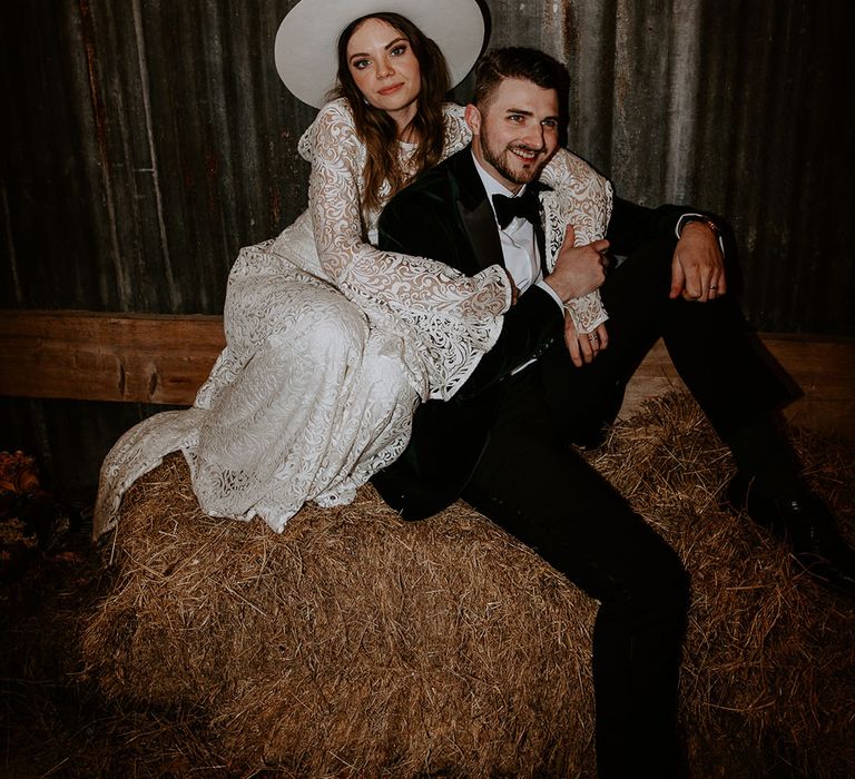 Bride in a boho wedding dress with a hat being hugged by the groom in a tuxedo 