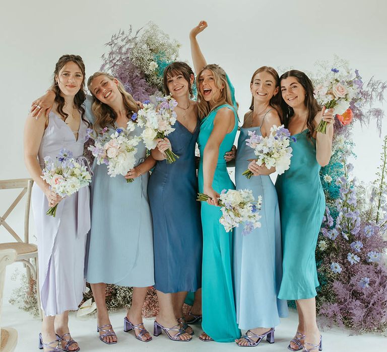 The bridesmaids all pose together in matching purple shoes in different colour bridesmaid dresses in all shades of blue 