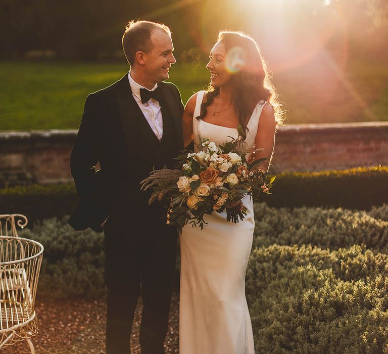 Golden hour wedding photography featuring Bride and Groom looking at each other and surrounded by greenery